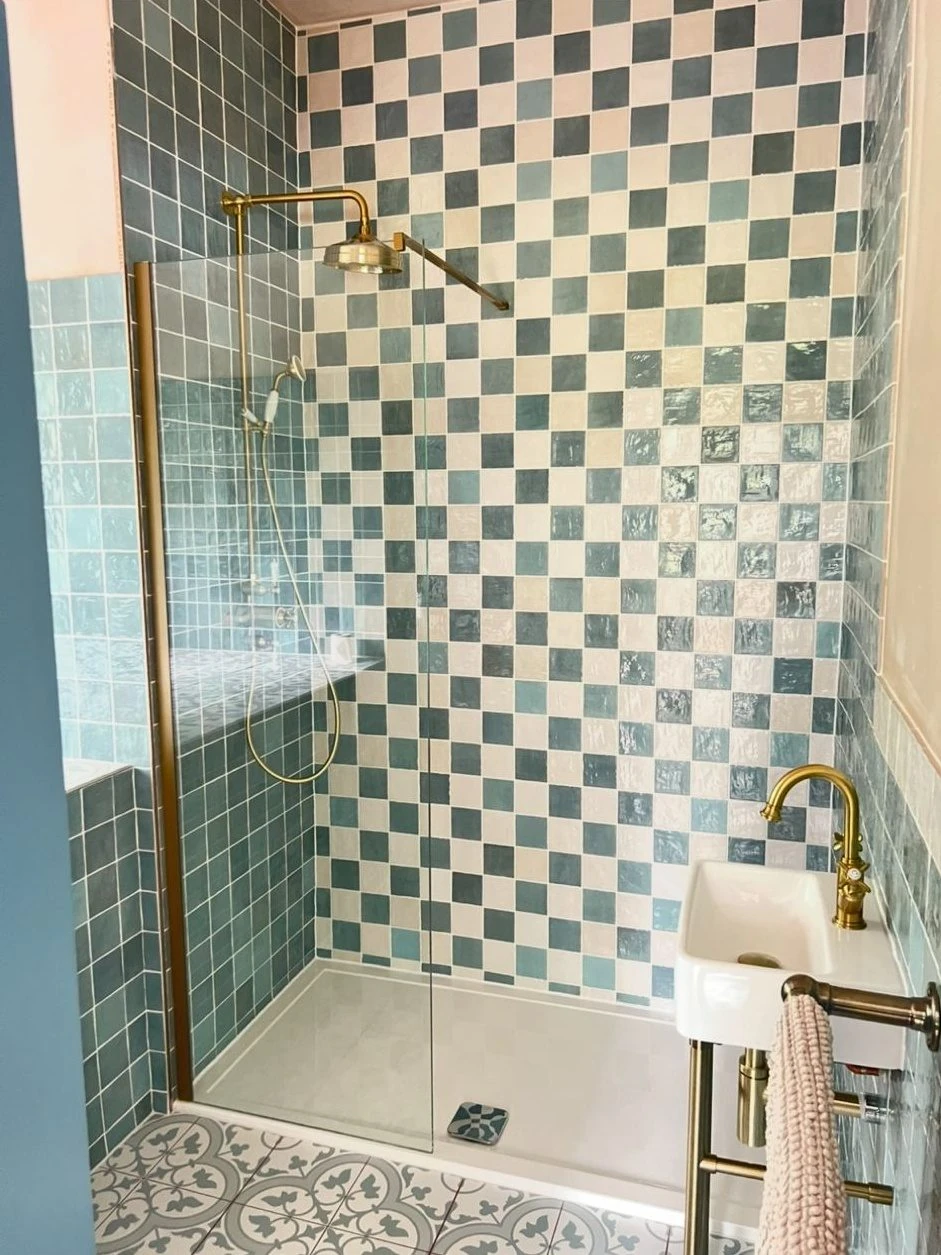 Walk-in shower with brass exposed shower, checkerboard tiles and patterned floor