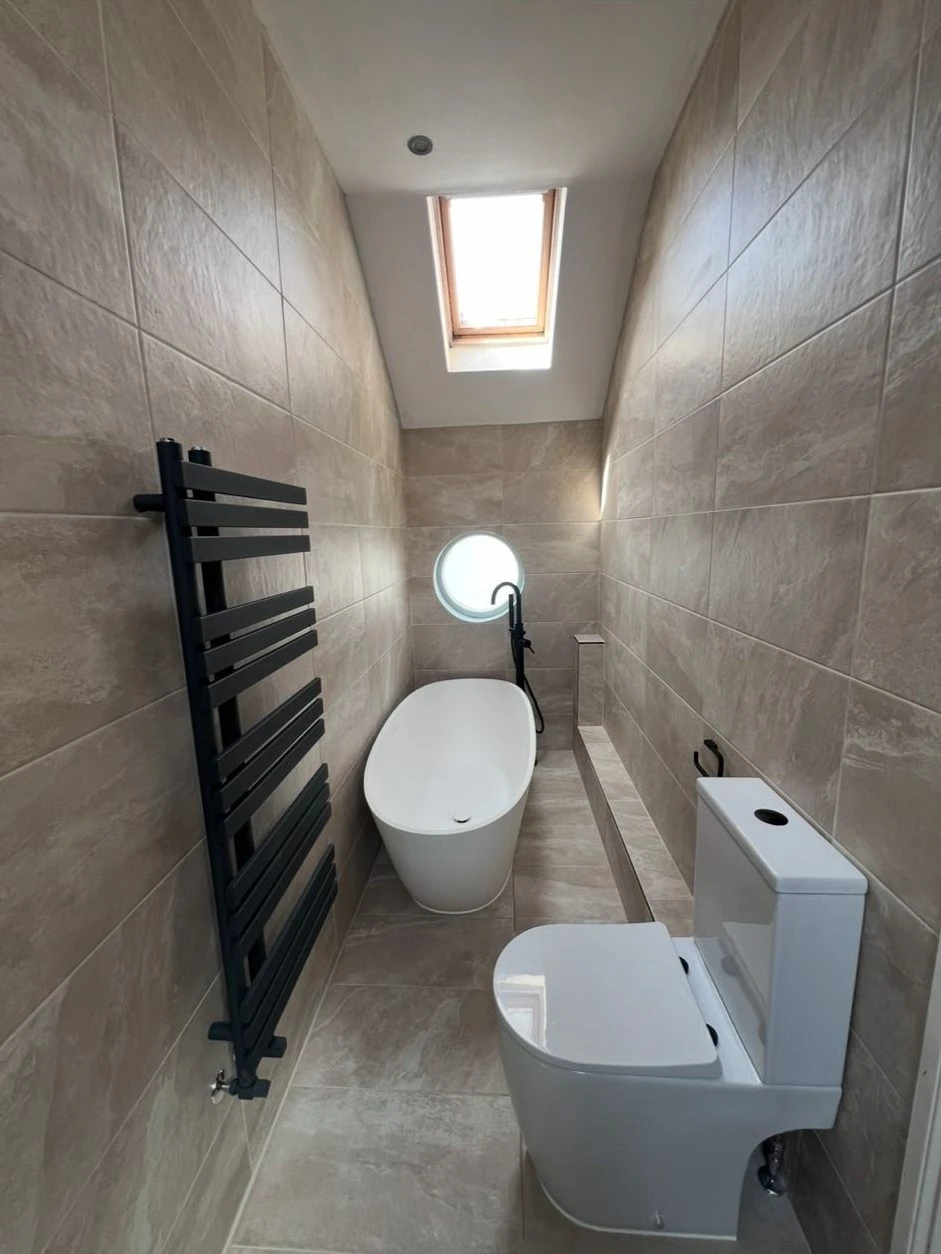 Loft bathroom installation with freestanding bath, black towel radiator and porcelain tiling