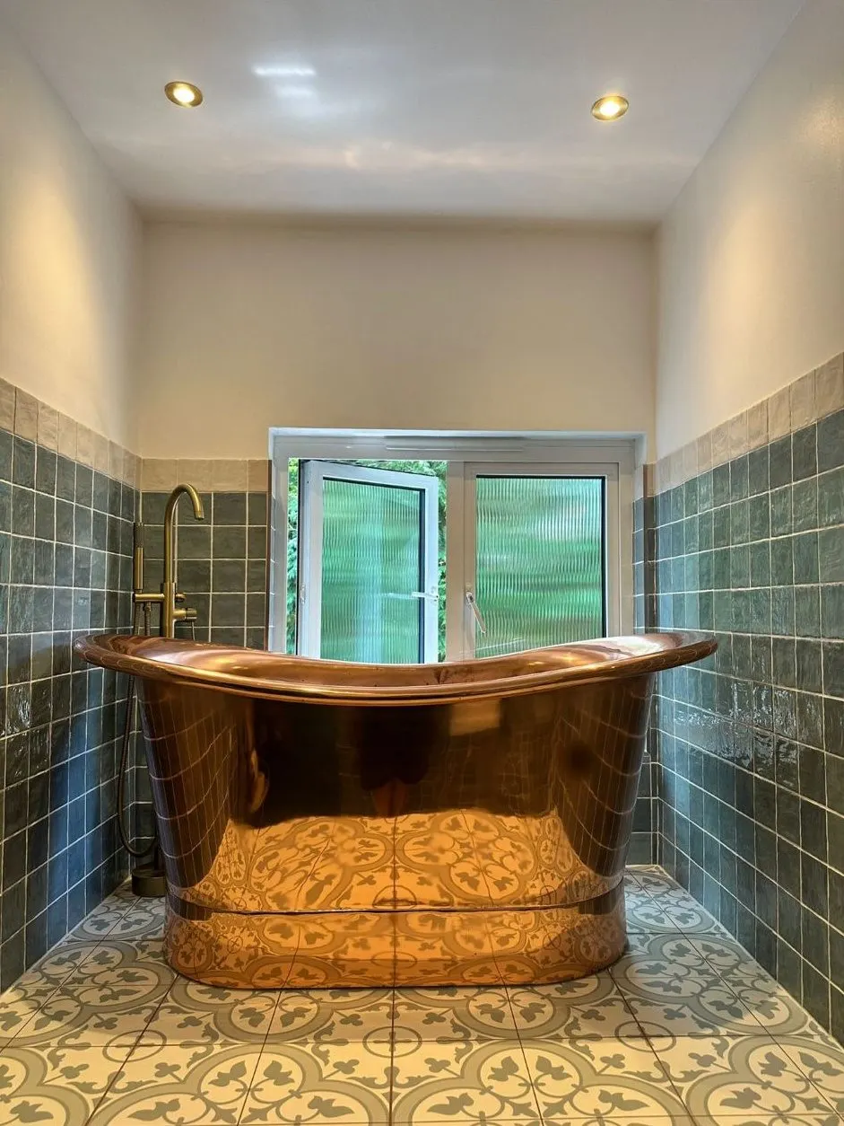 Freestanding copper bath with floor-standing brass tap and patterned floor tiles, bathroom installation Reading