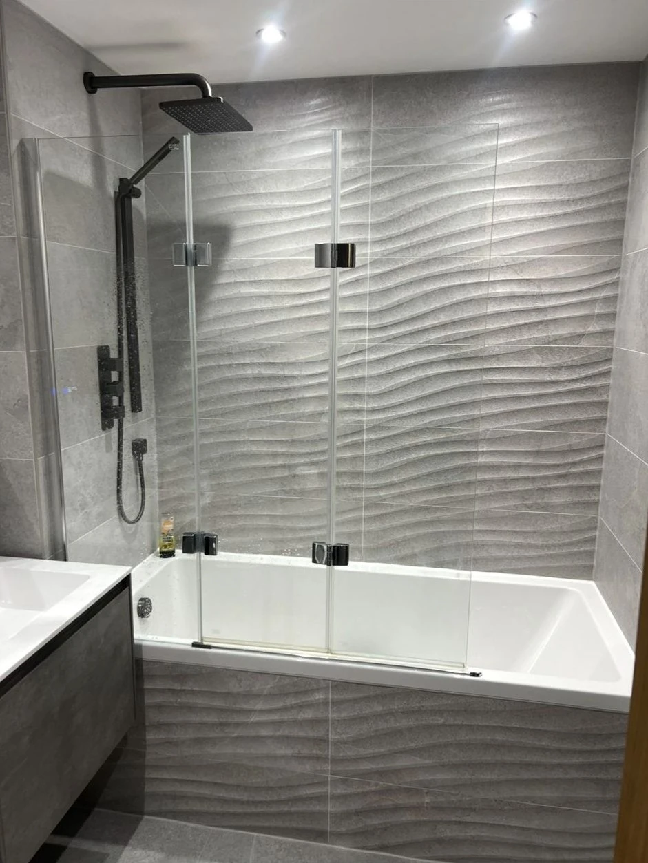 Bathroom refit with wave-textured tiles, folding bath screen and matt black shower valve