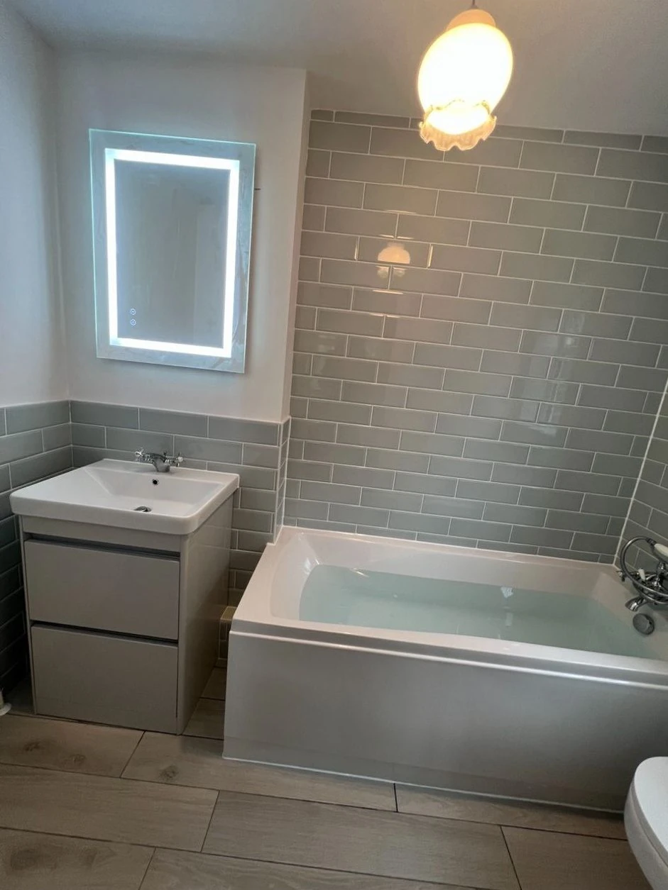 Bathroom installation with metro wall tiles, bath, vanity basin and illuminated mirror