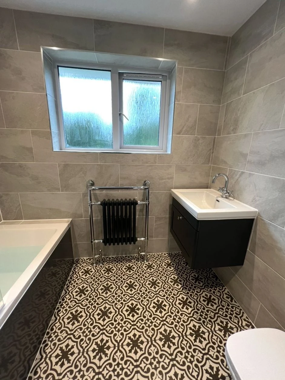 Refitted bathroom with patterned floor tiles, traditional towel radiator and wall-hung basin unit