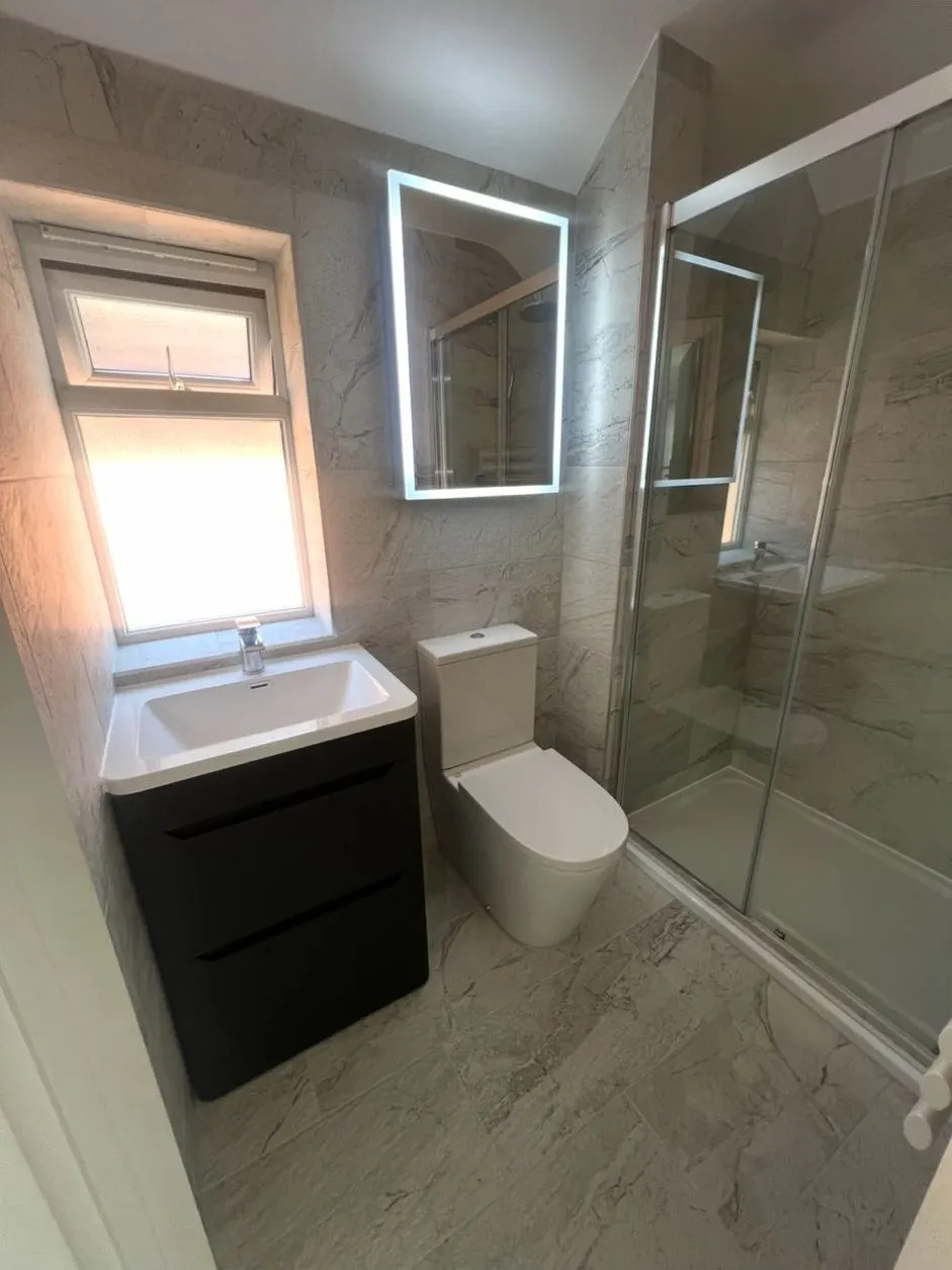 Compact bathroom installation with sliding-door shower enclosure, vanity unit and LED mirror