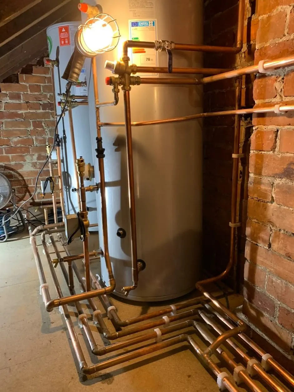 Copper plumbing pipework runs neatly clipped around twin hot water cylinders in a loft