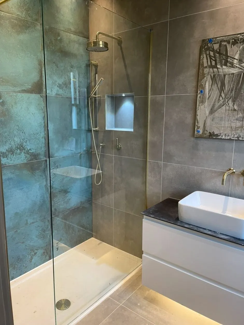 Walk-in shower installation with brushed brass rainfall head, recessed niche and large-format tiles