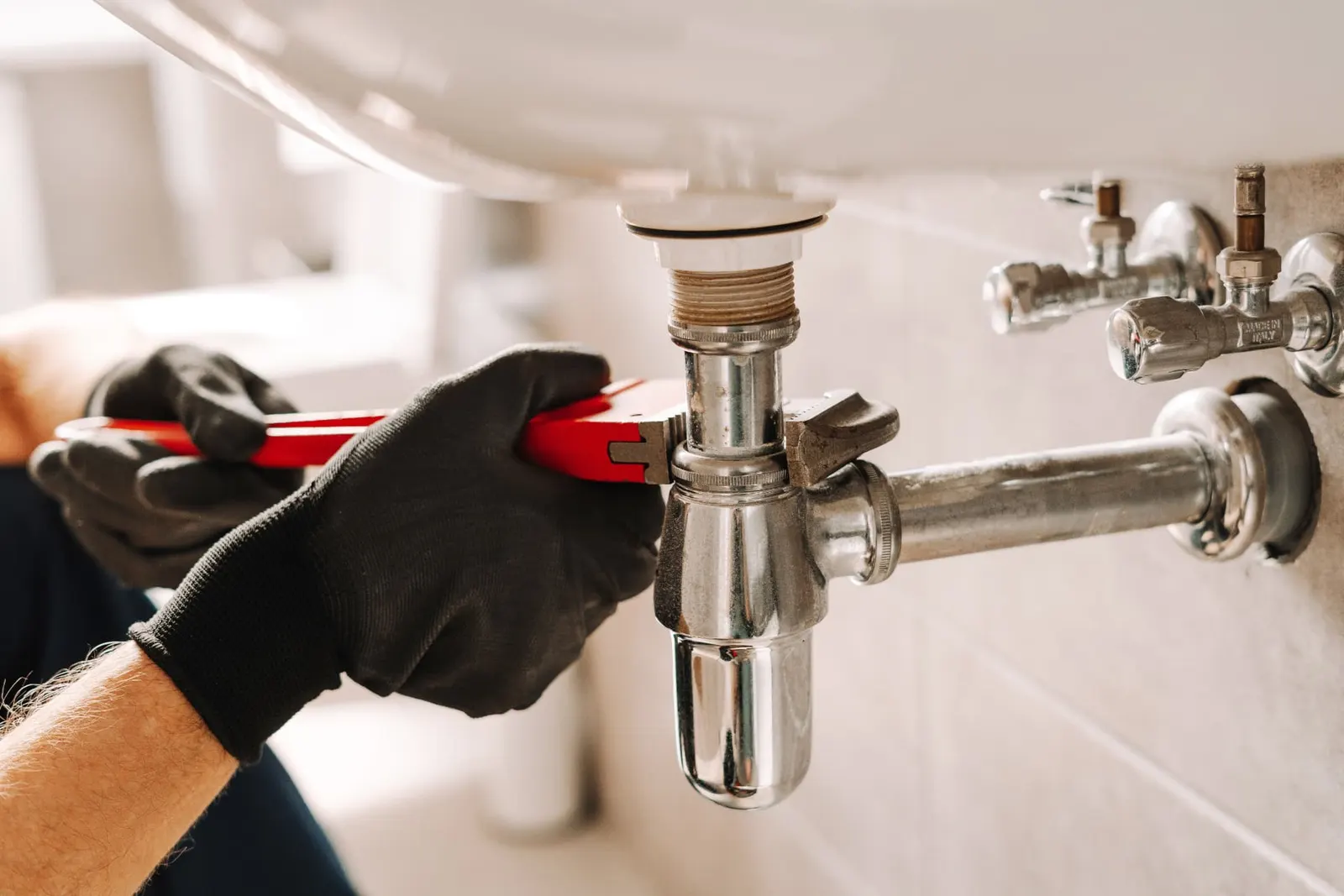 Plumber tightening a basin trap with a pipe wrench during an emergency plumbing call-out in Reading