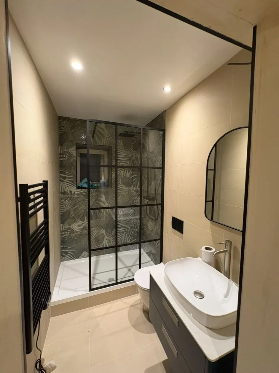 Shower room with black grid shower screen, tropical leaf feature wall and arched mirror