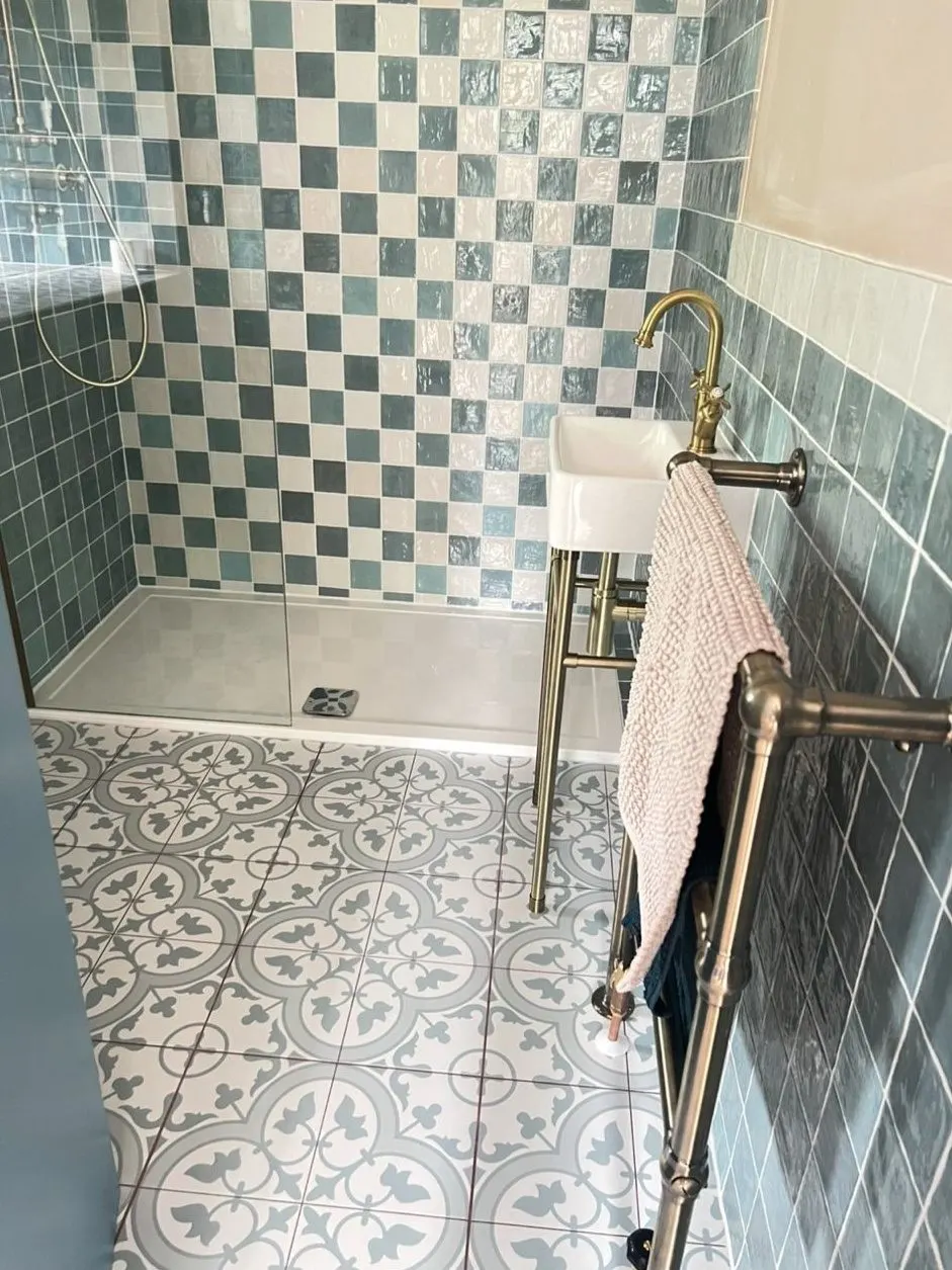 Shower installation with blue-green square wall tiles, brass shower and patterned floor