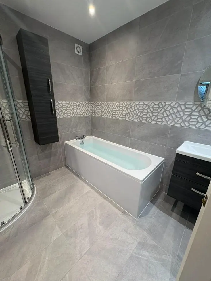 Grey tiled family bathroom with straight bath, quadrant shower enclosure and wall cabinet
