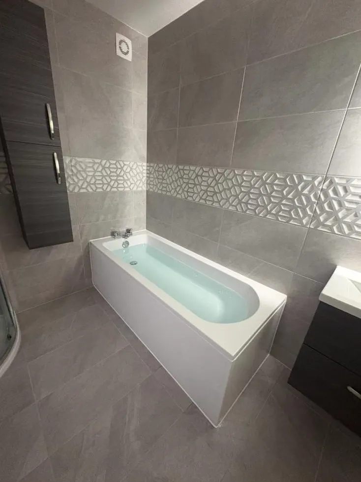Bathroom installation in Reading with white bath, dark vanity unit and patterned tile feature strip